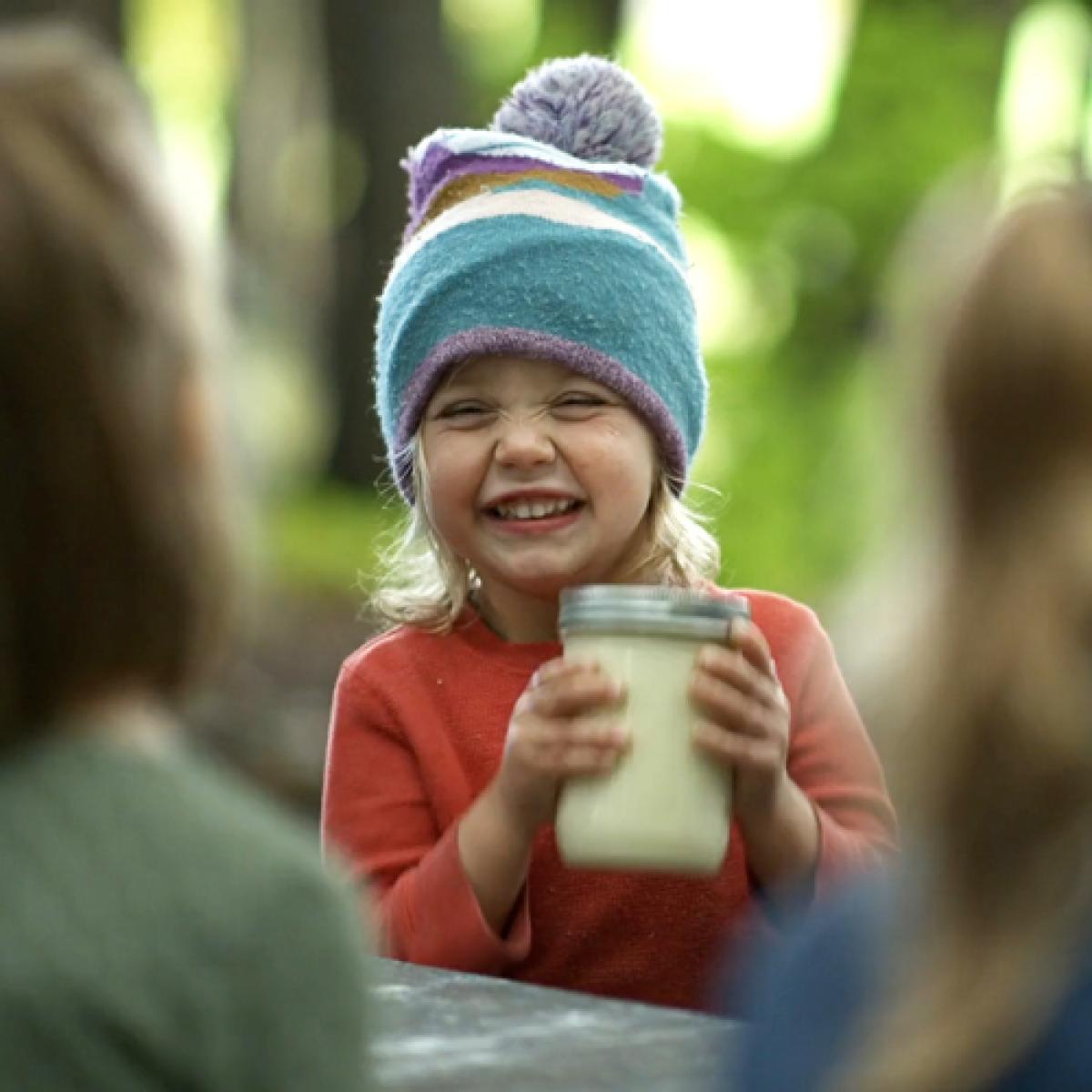 A child smiles as she shakes a jar of cream, turning it to butter.