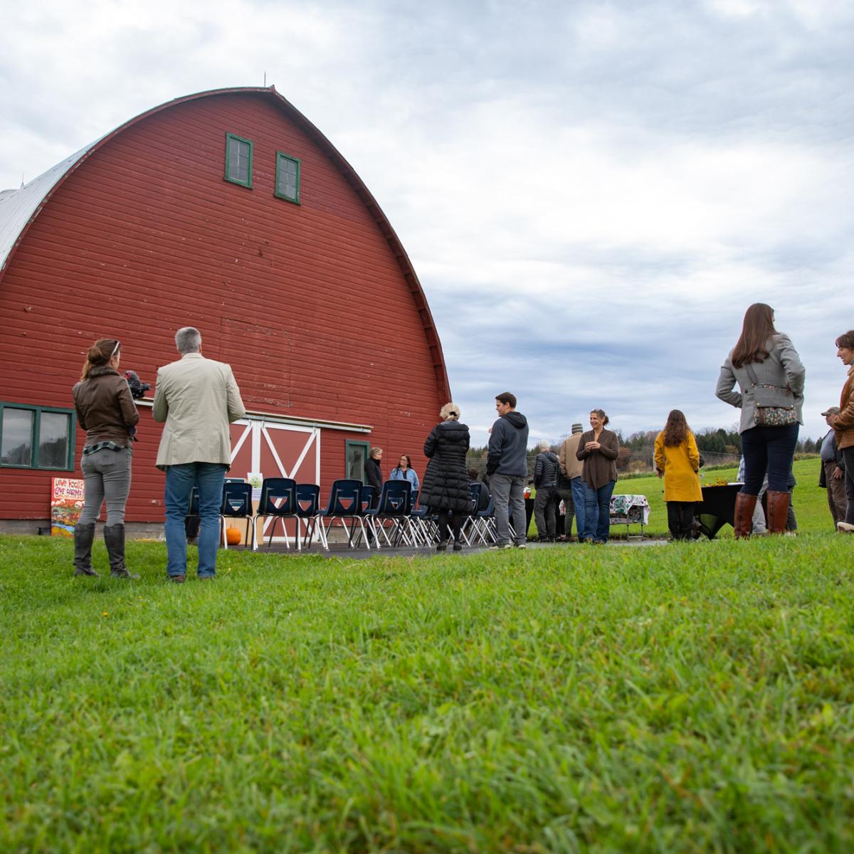 A red barn on school grounds, people gathered for a farm to school event
