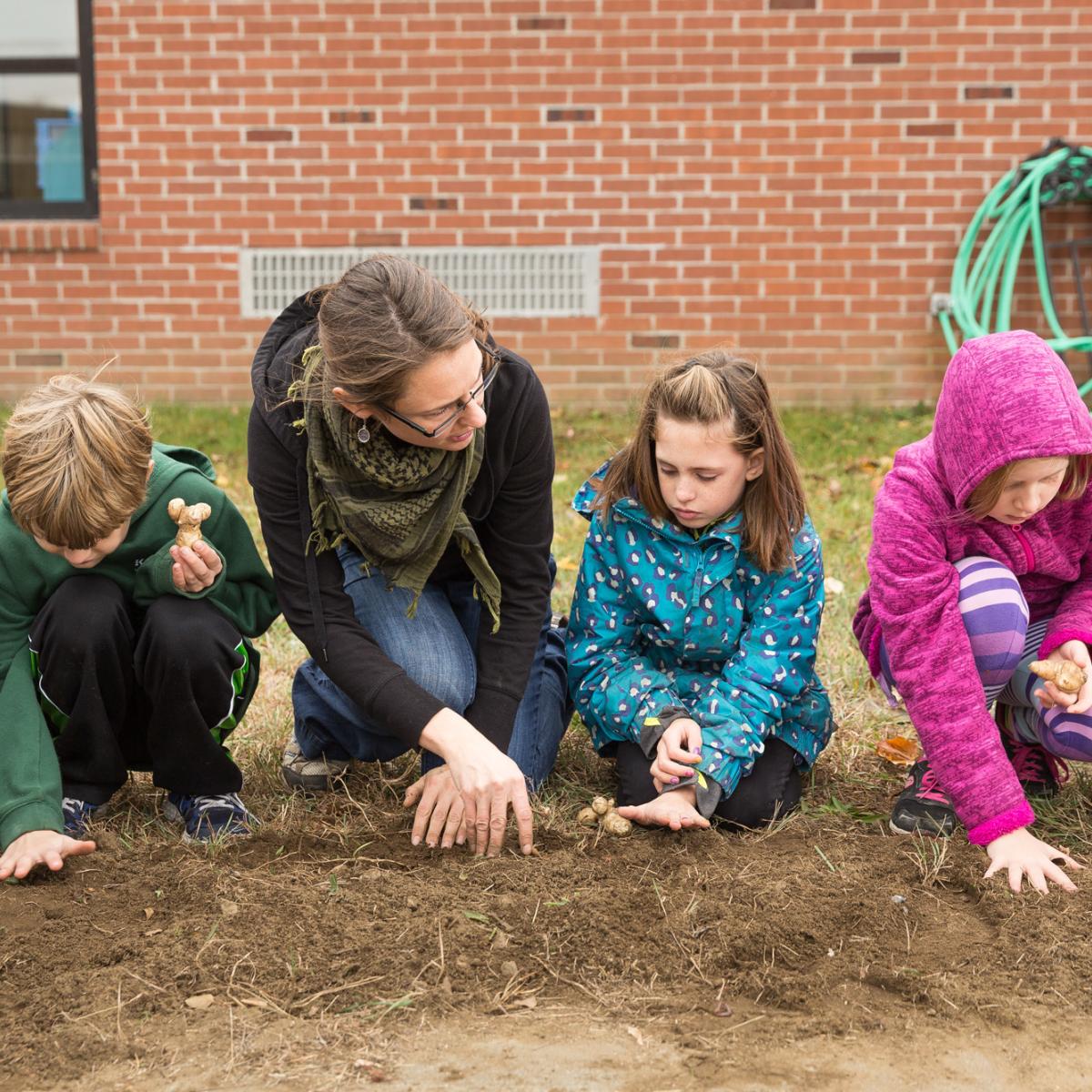 students and a teacher outdoors with the hands in soil