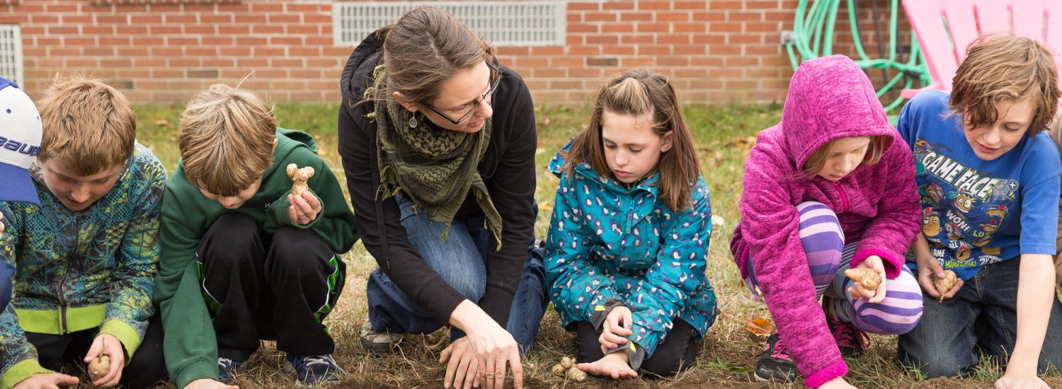 students and a teacher outdoors with the hands in soil