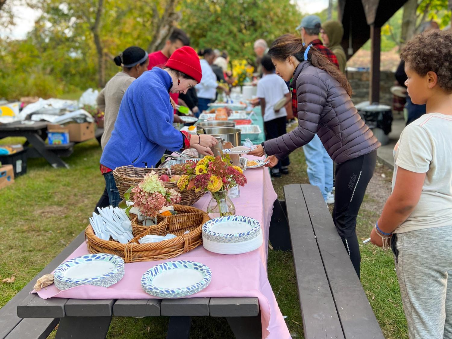 People line up at picnic tables, full of plates of food to share
