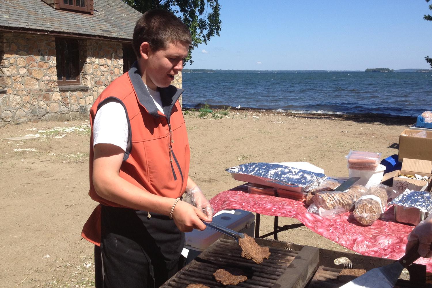 A young man grills hamburgers outdoors