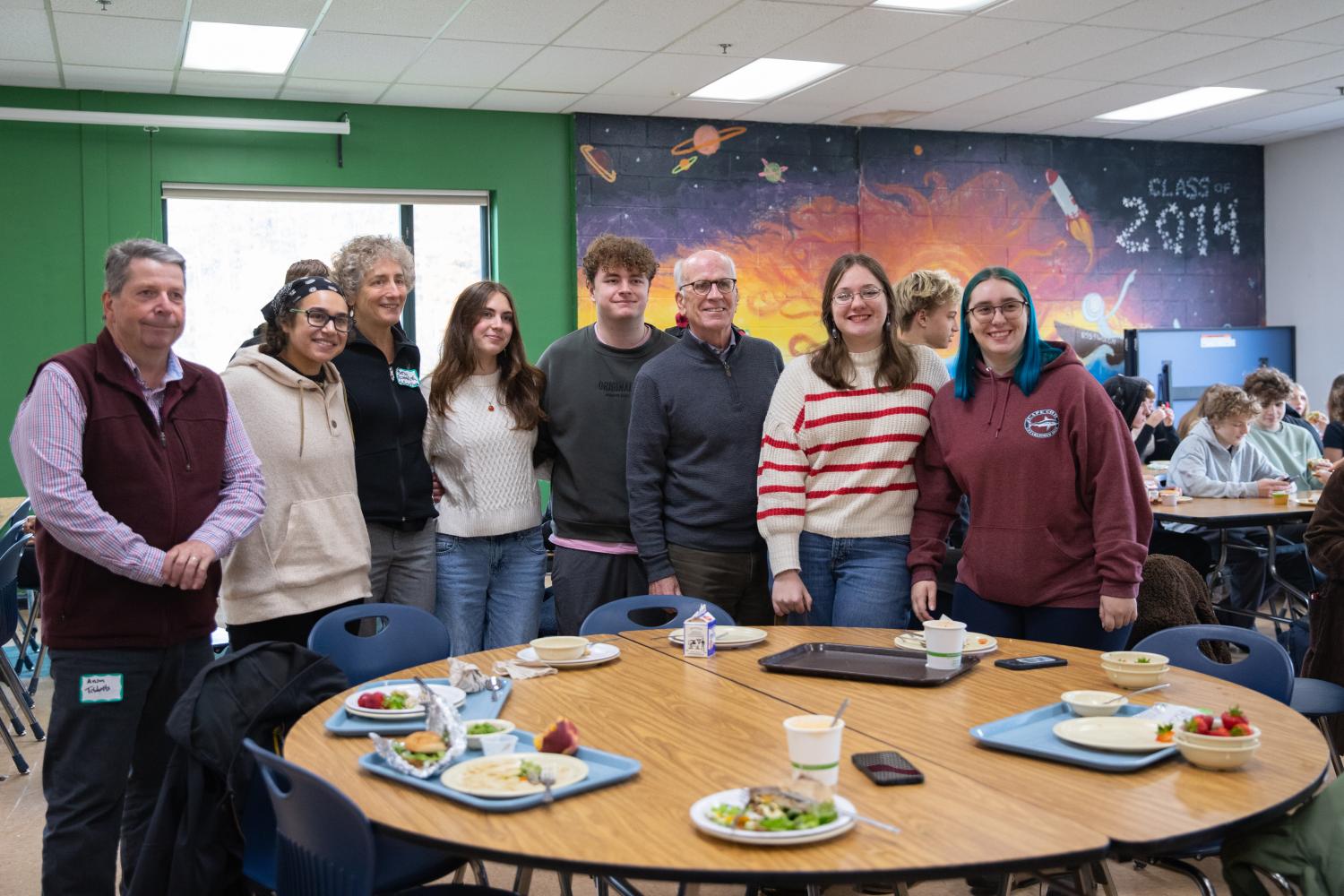 US Senator Peter Welch stands with four students in front of a mural with a space theme, smiling at the camera.