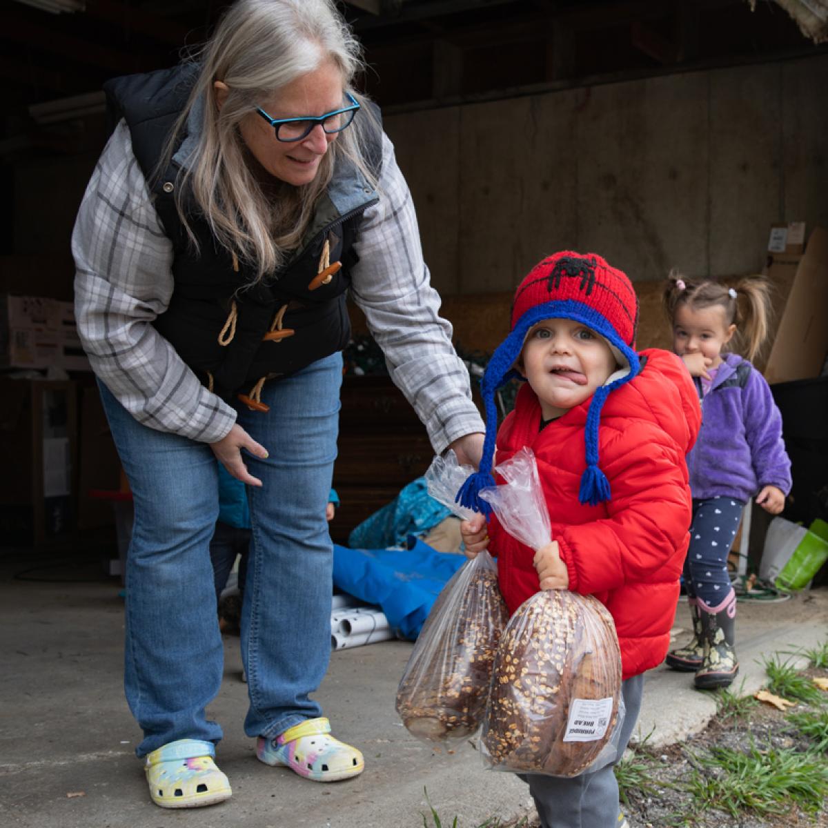 Laura Butler encourages one of the children as he carries loaves of bread from the farm truck to the neighborhood CSA pickup table.