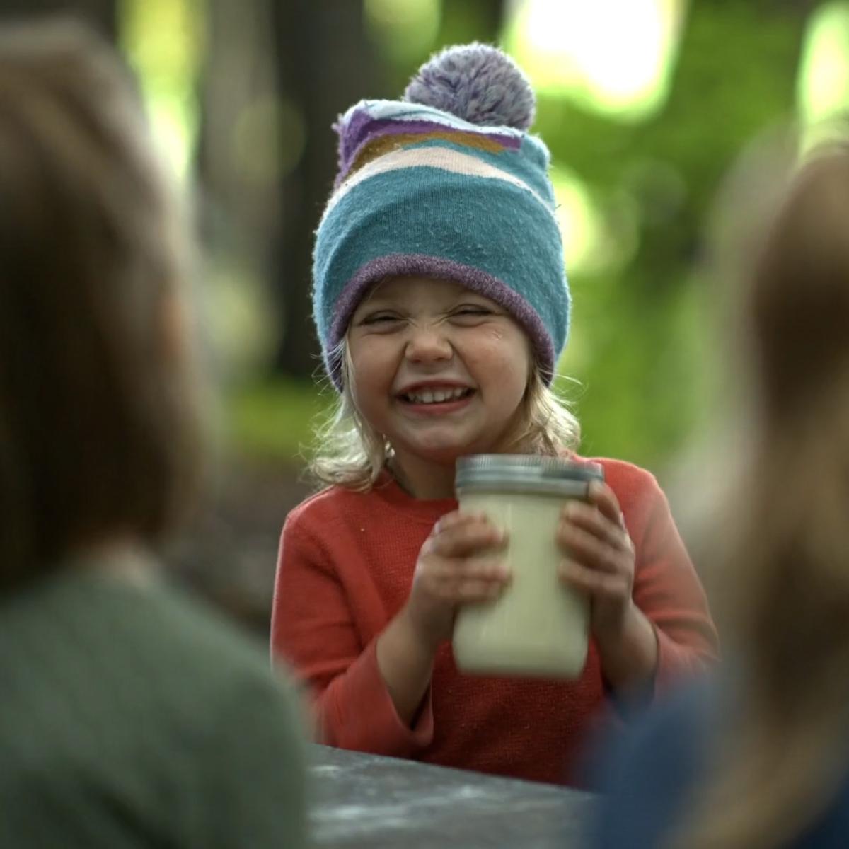 A child smiles as she shakes a jar of cream, turning it to butter.