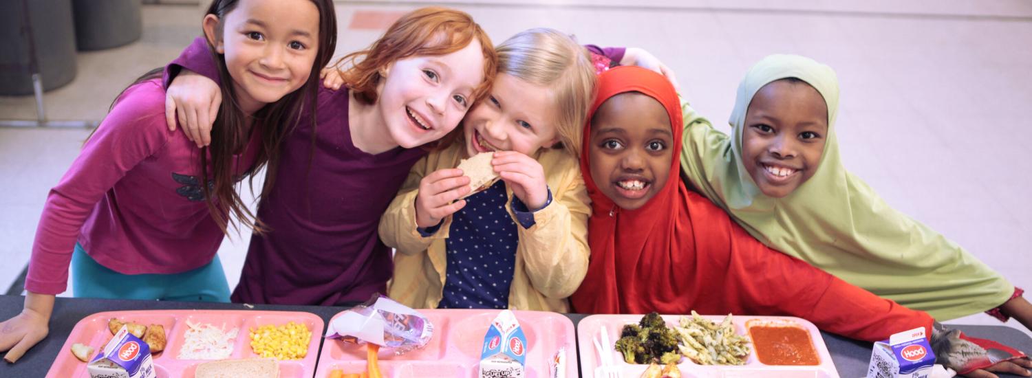 Five young students enjoy school meals in the cafeteria.