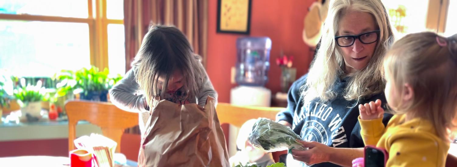 An educator and young kids unpack a bag of fresh vegetables.