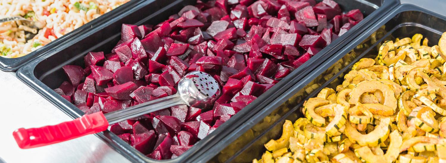 Trays of colorful rice, beets, and squash on a school lunch serving line